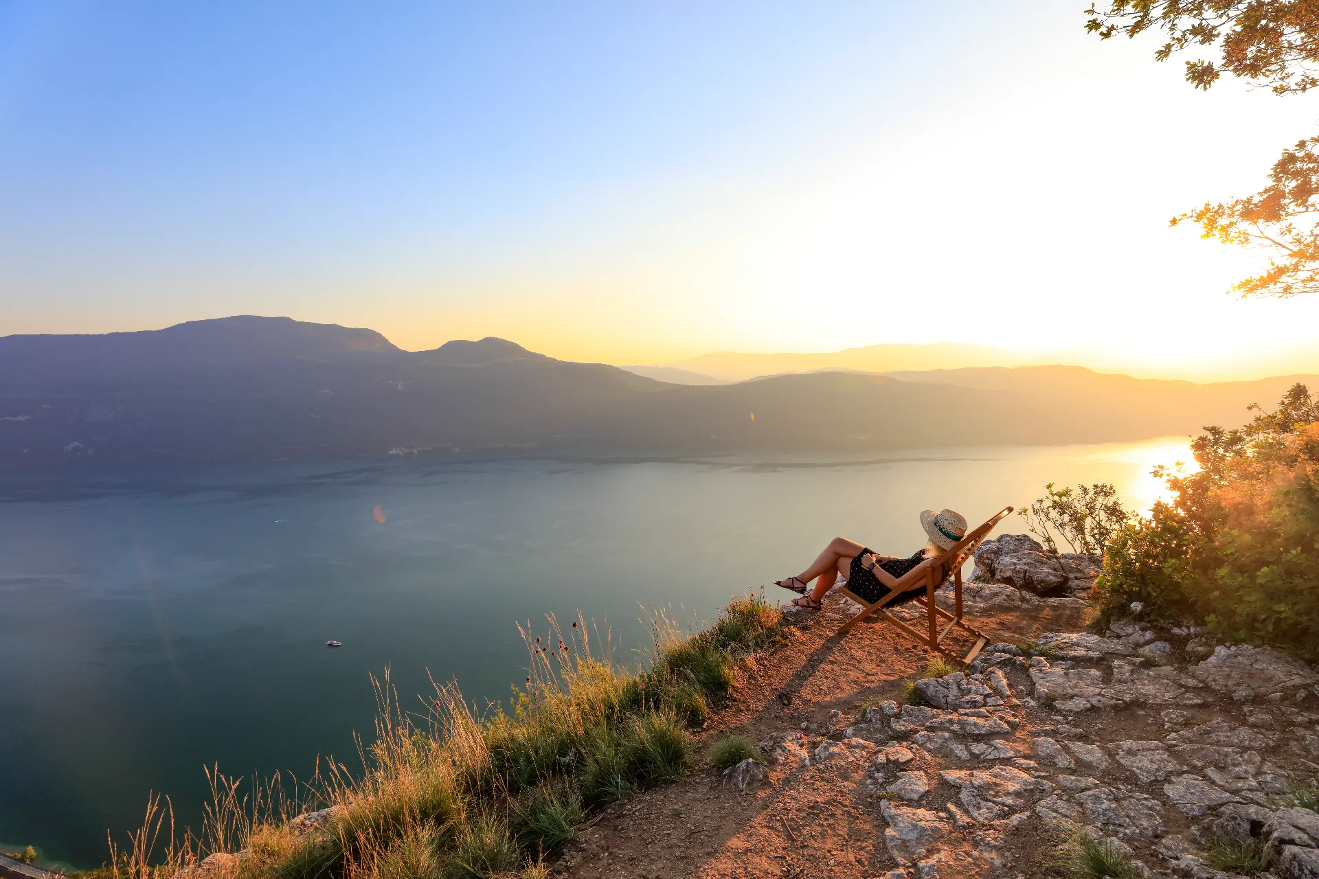 Randonnée en famille autour du petit camping en Savoie-Coucher de soleil sur le Lac du Bourget, avec une jeune dame se relaxant sur un transat, profitant de la vue panoramique sur le lac.